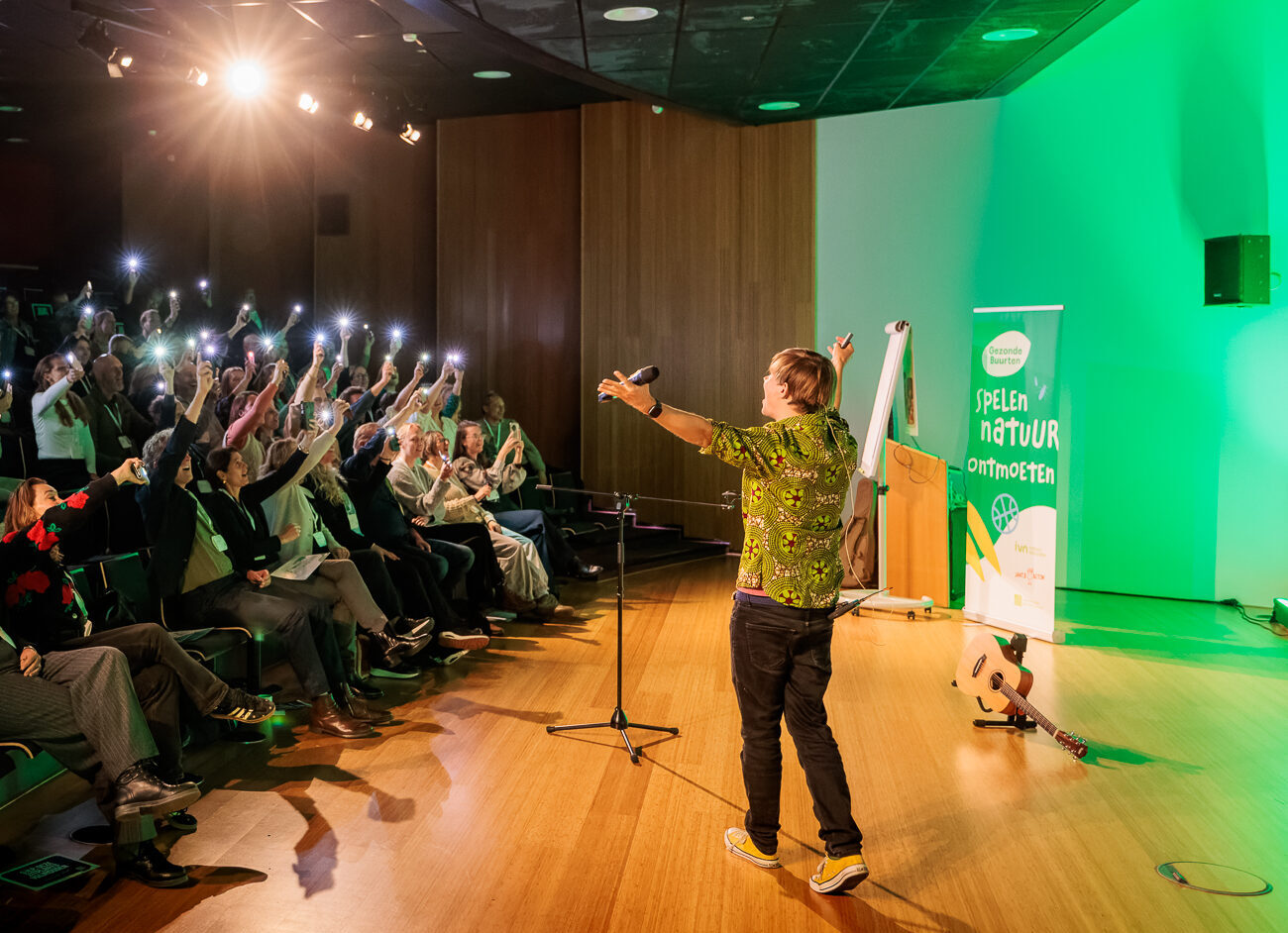 Een spreker op het podium met publiek dat telefoons omhoog houdt als lampen.