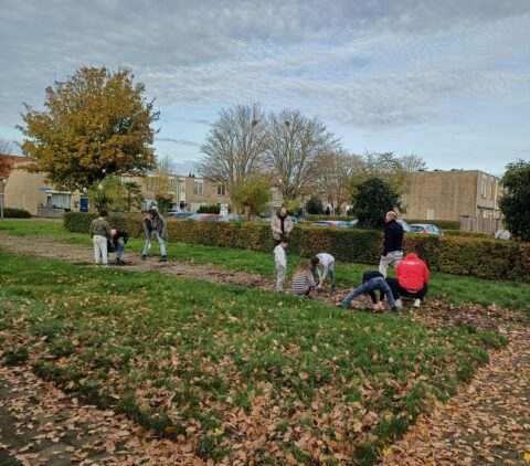 Mensen planten bollen in een herfstig park, omringd door huizen en kale bomen.