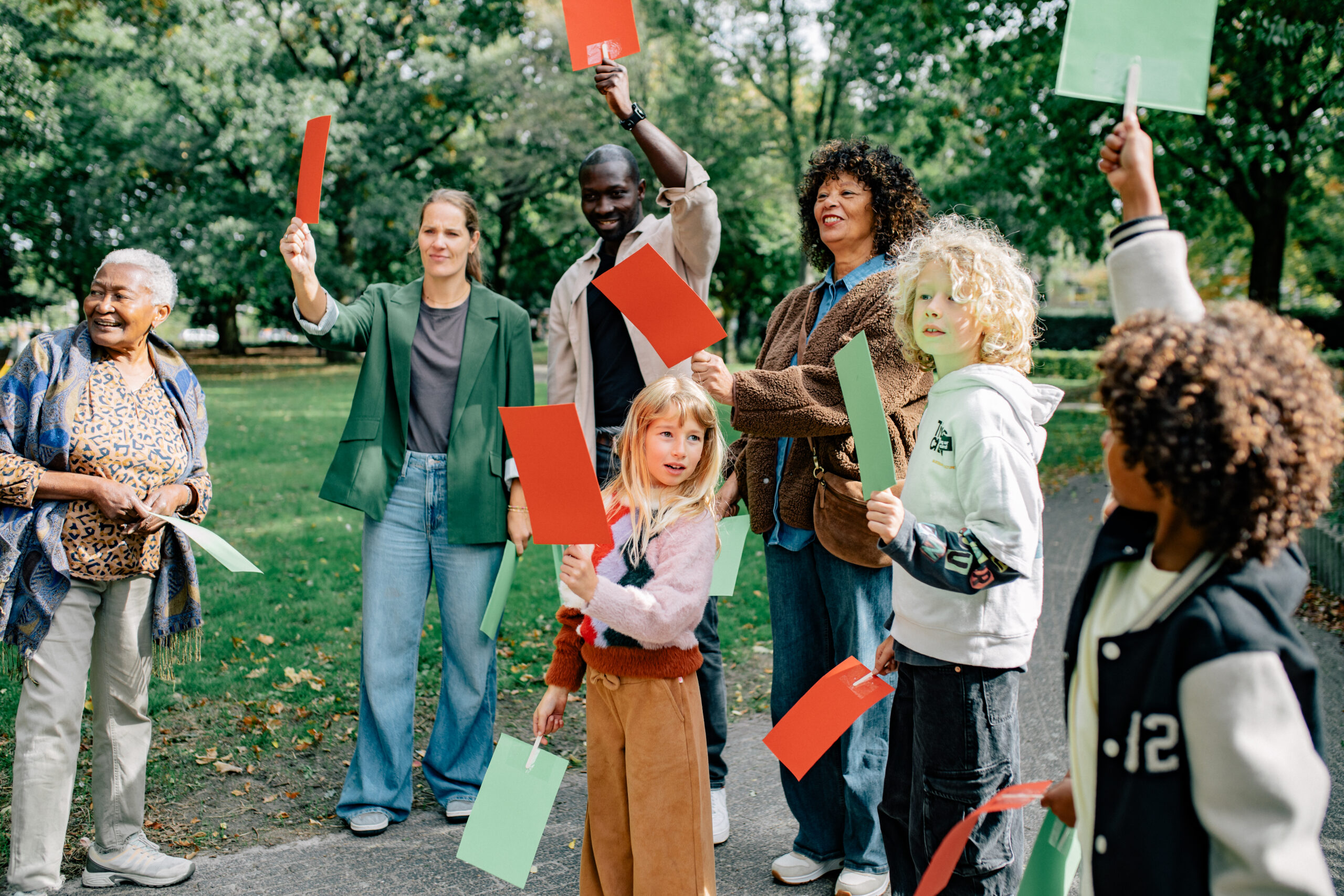 Groep mensen in een park die gekleurde kaarten omhoog houden tijdens een activiteit.