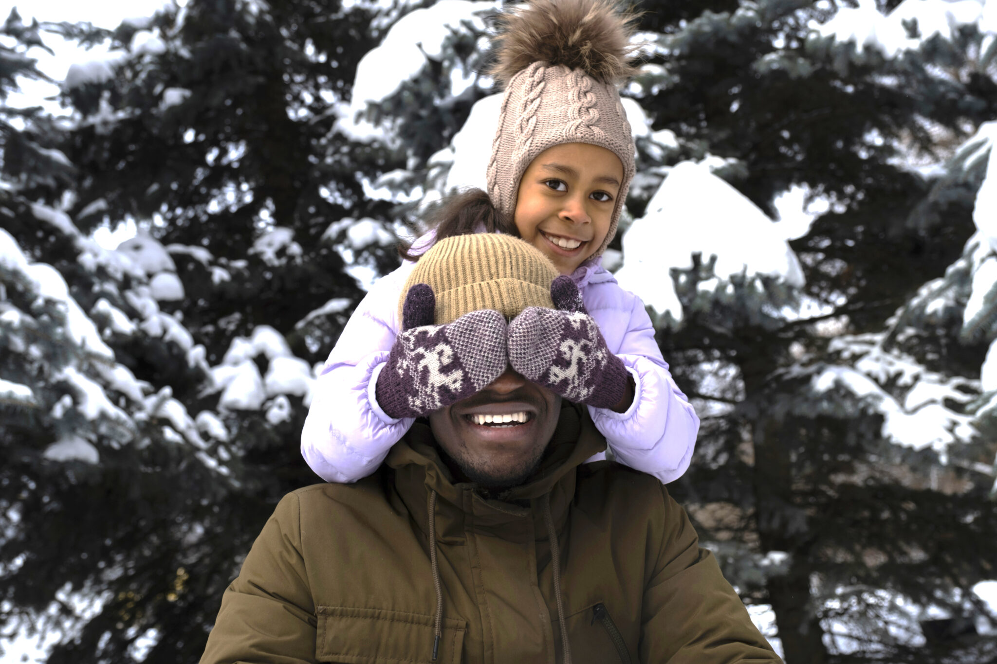 Kind bedekt glimlachende man zijn ogen met wanten in besneeuwde omgeving.