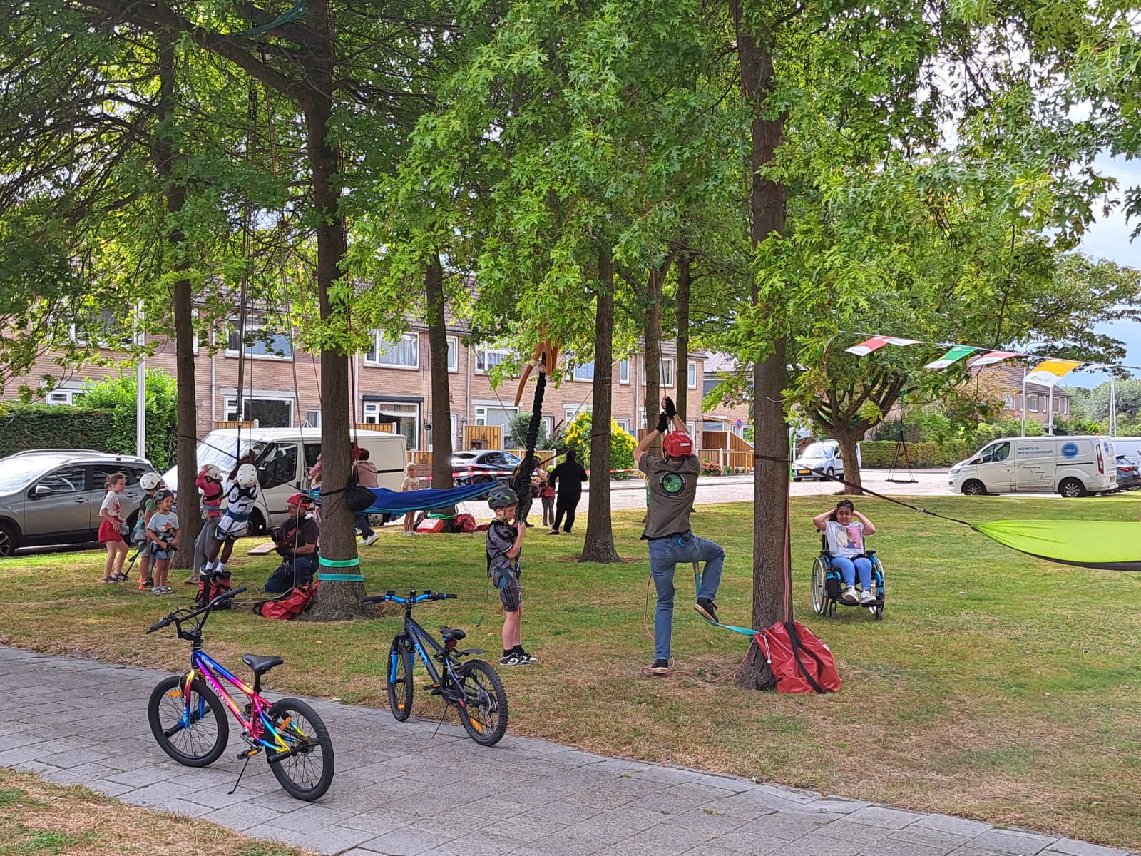 Kinderen spelen in het park met fietsen en schommels, omgeven door bomen en vlaggetjes.