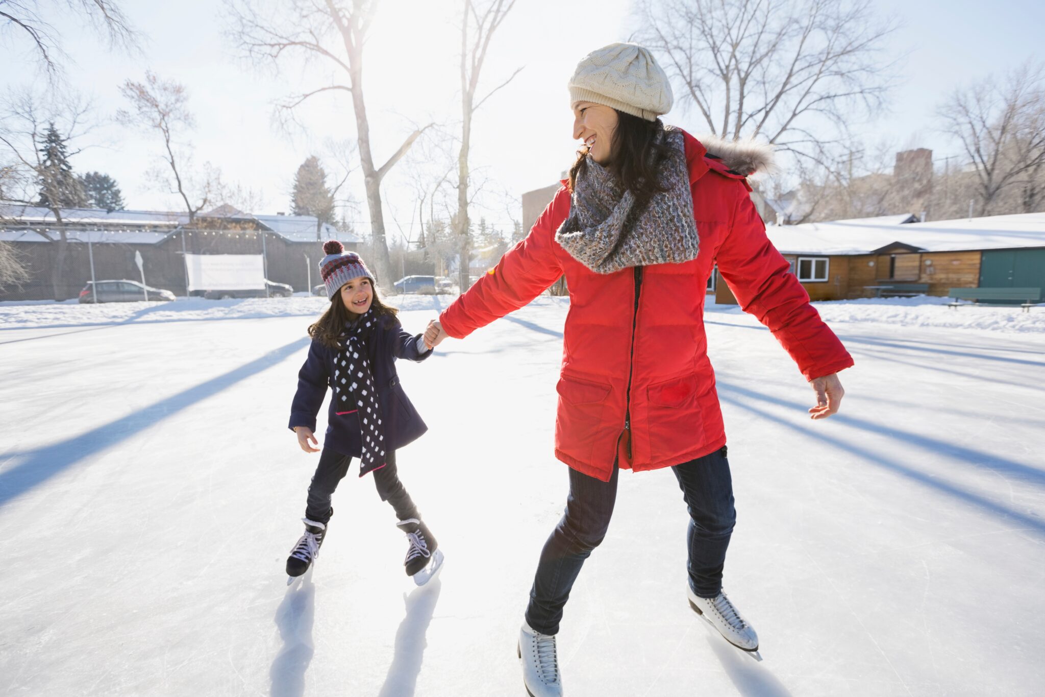 Moeder en dochter schaatsen samen op een zonnige dag in een winterlandschap.