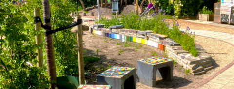 Mozaïekbankjes in een kleurrijke tuin met stenen en planten langs een slingerend pad.