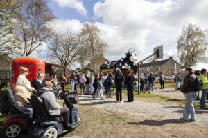 Mensen bij een evenement met een rode voedselkraam en een springkussen in de vorm van een koe.