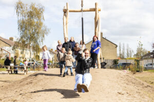 Een groep kinderen speelt buiten op een kabelbaan onder een heldere hemel.
