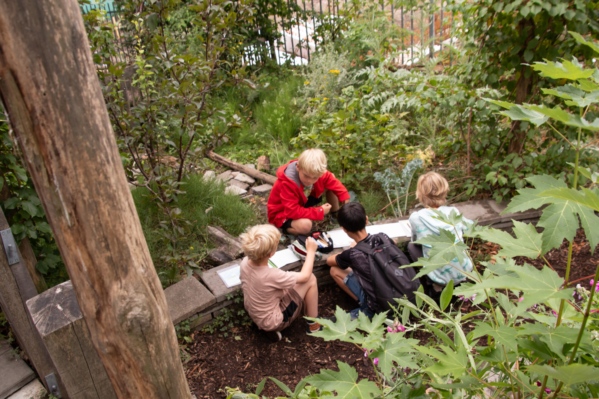 Vier kinderen zitten in een tuin en werken samen aan hun schoolwerk.