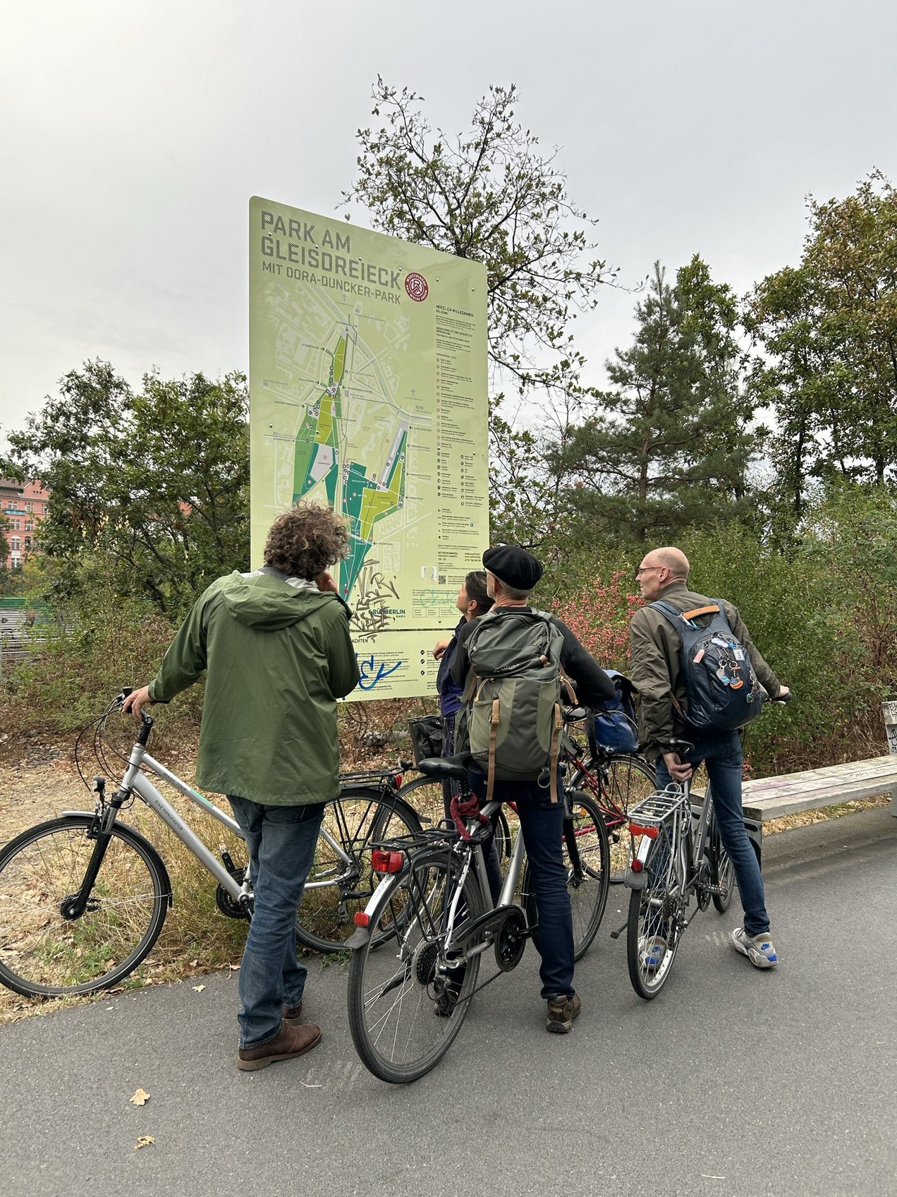 Fietsers bekijken een plattegrond van Park am Gleisdreieck, omringd door bomen.