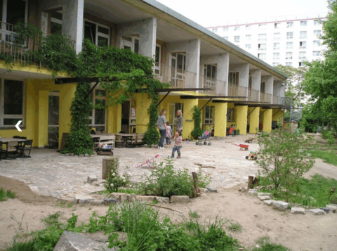 Appartementencomplex met binnenplaats, spelende kinderen en ouders, omringd door groen en speelgoed.