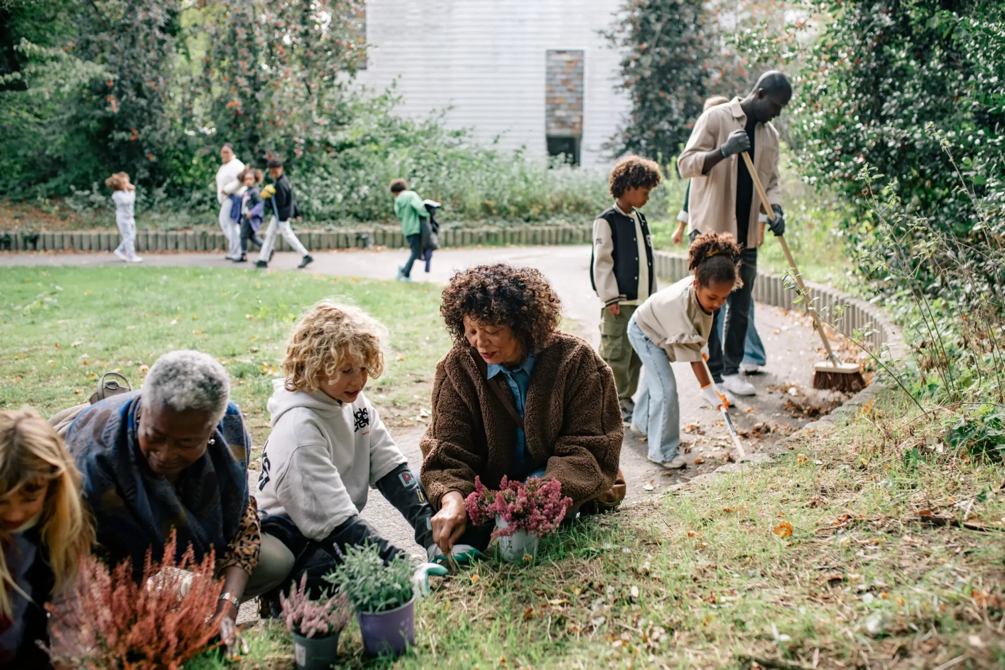 Mensen tuinieren samen in een park, planten bloemen en vegen bladeren.