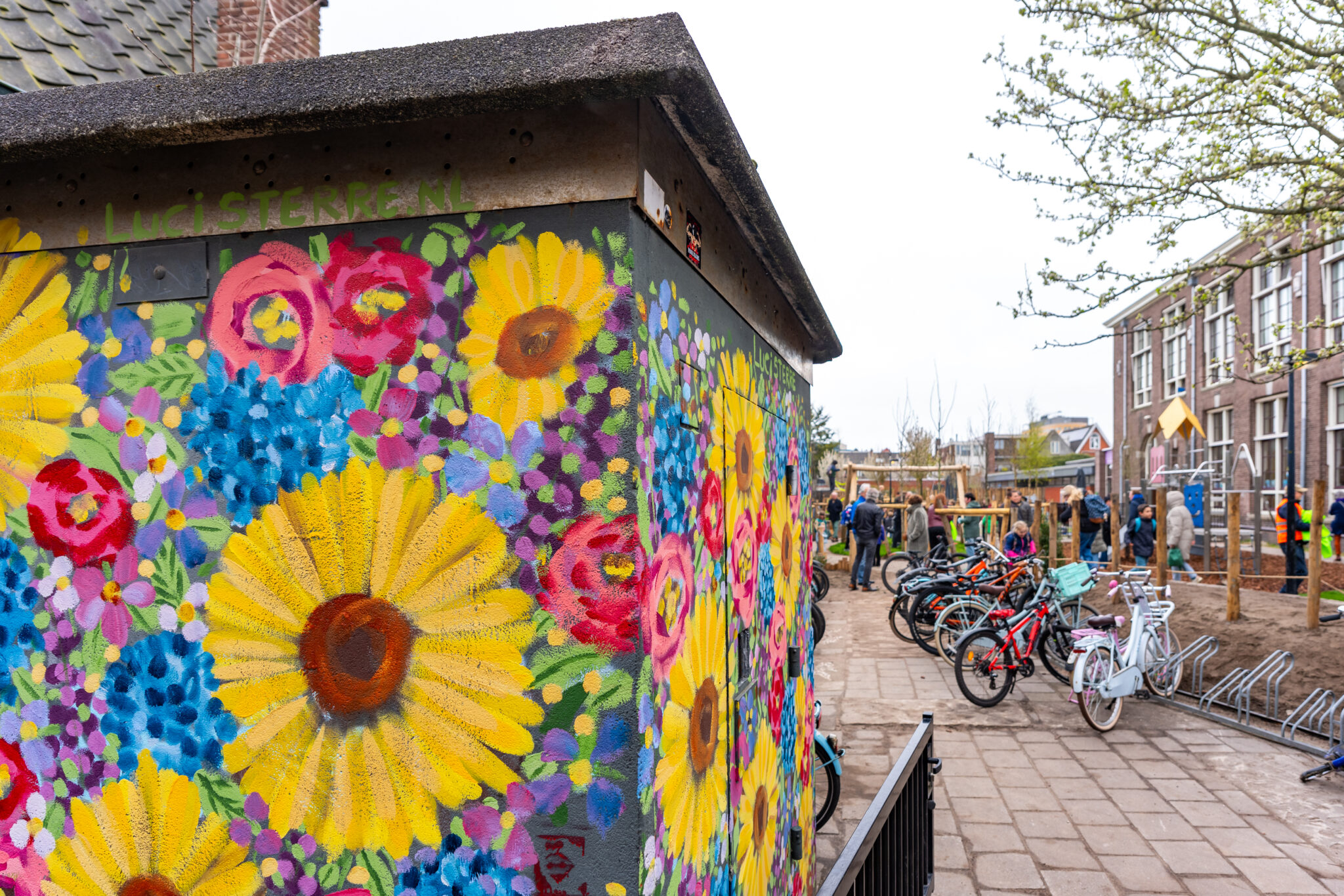 Felle bloemenmuurschildering, nabij fietsenrek en schoolplein met spelende kinderen.