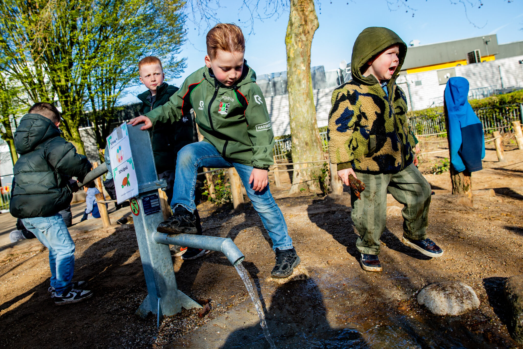 Kinderen spelen bij een waterpomp op een zonnige dag in een speeltuin.