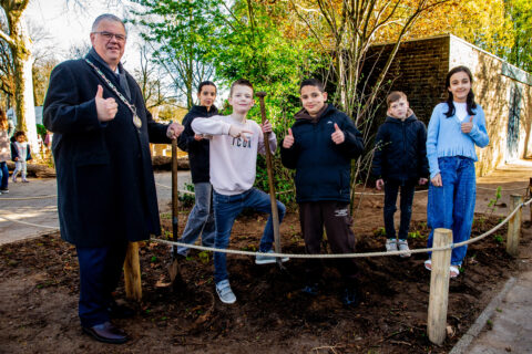 Volwassen man en vijf kinderen planten een boom en steken duimen op in een tuin.