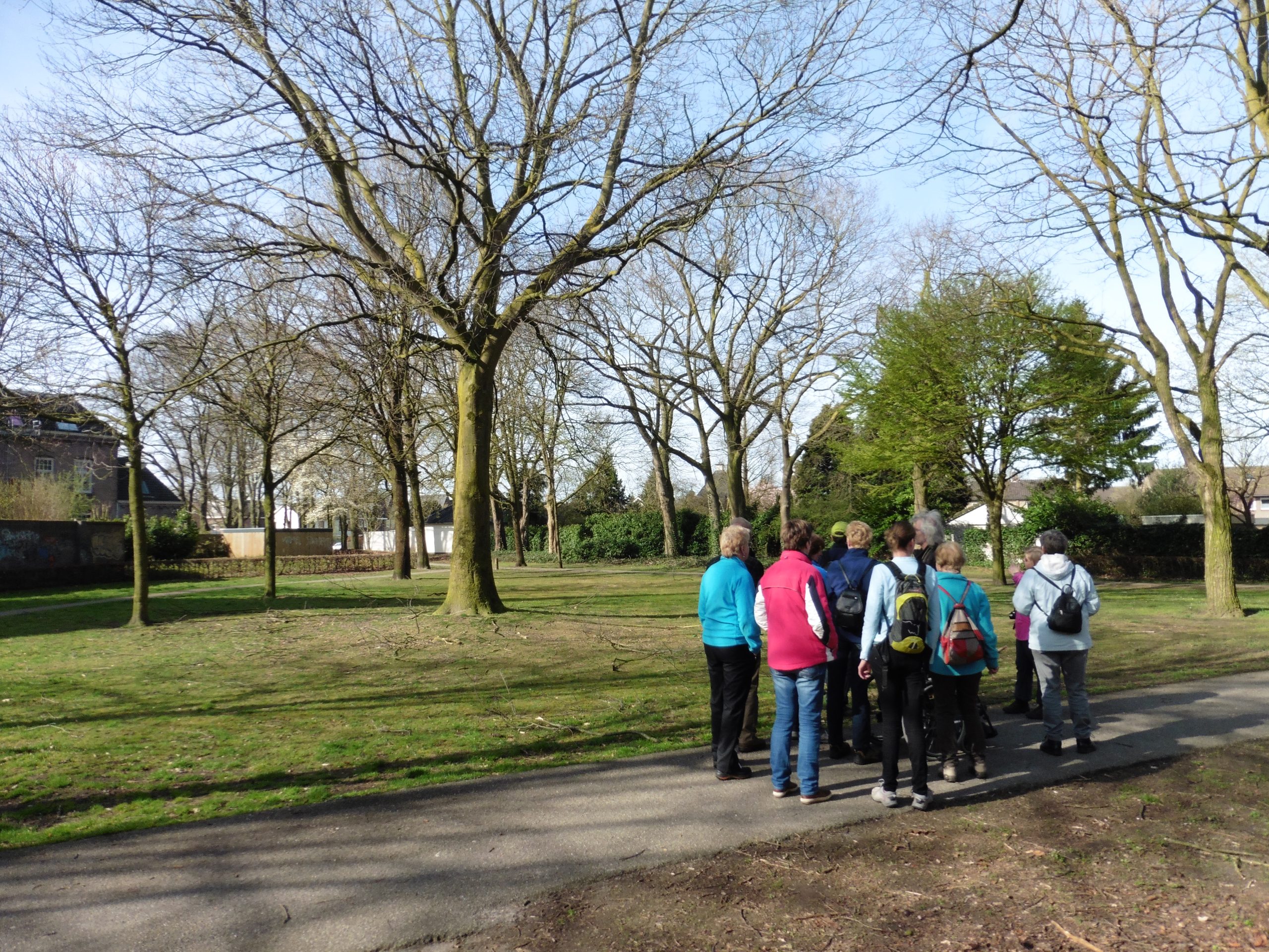 Een groep mensen wandelt op een pad in een groen park met kale bomen.