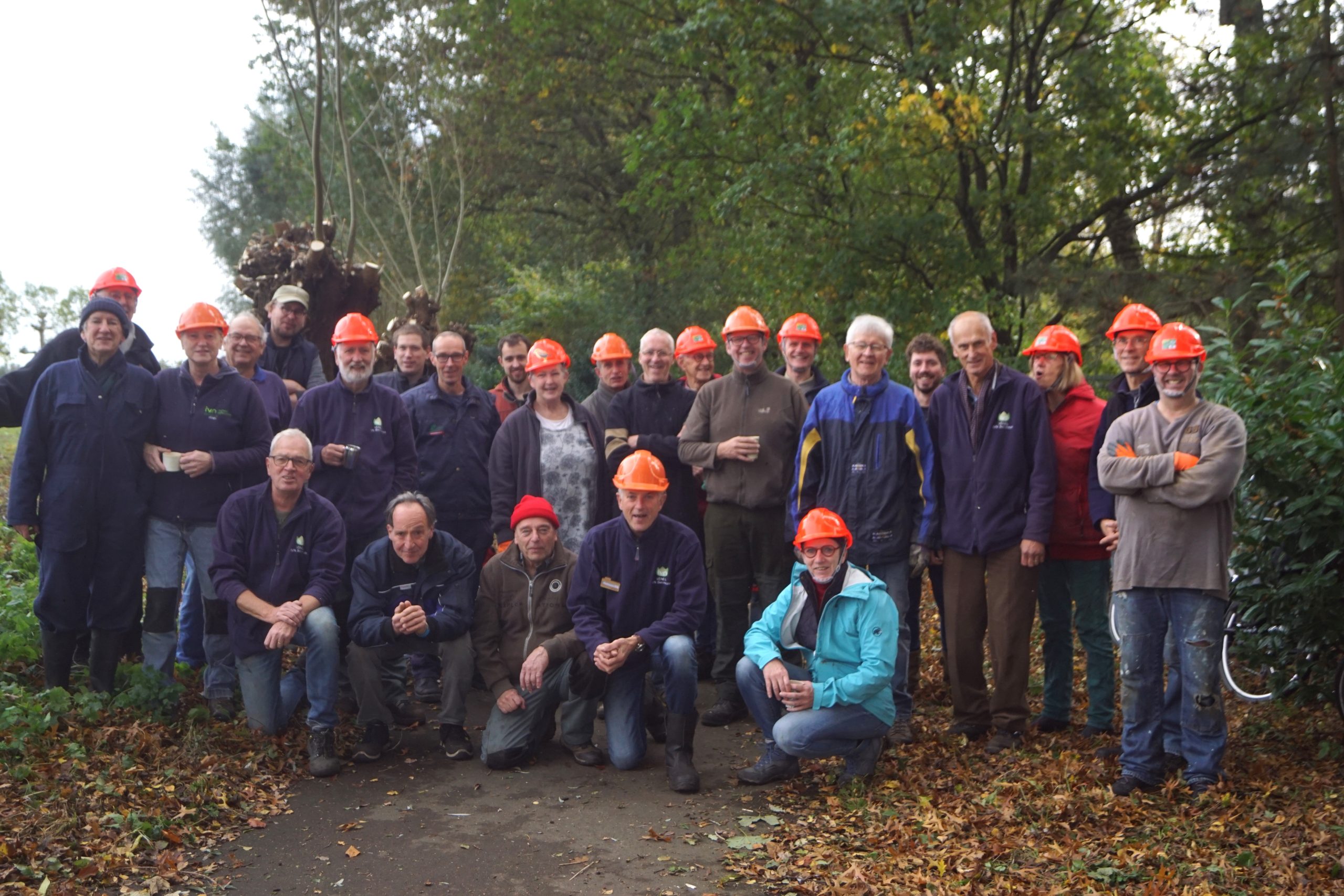 Groep mensen met helmen in een bosrijke omgeving, poseren voor een foto.