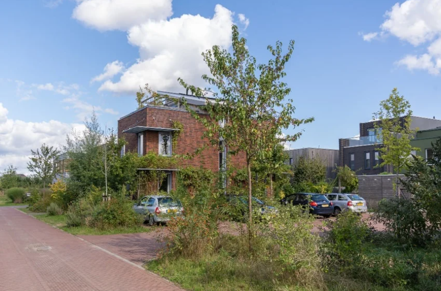 Rode bakstenen huizen met geparkeerde auto's en groene bomen onder blauwe lucht.