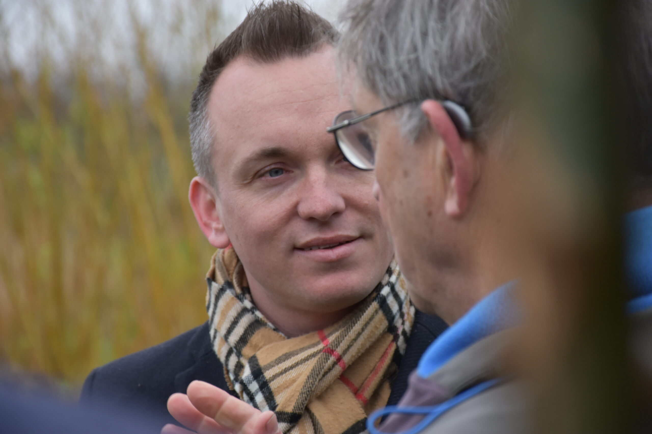 Twee mannen in gesprek buiten, één draagt een geruite sjaal en kijkt de ander aan.