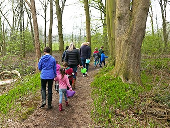 Groep kinderen met begeleiders wandelt door een bos op een modderig pad met emmers.