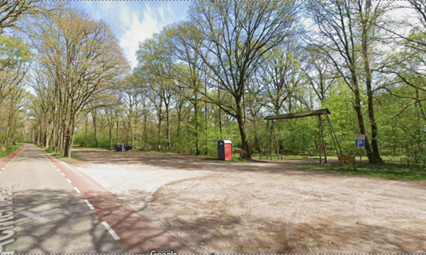 Bosrijke parkeerplaats met een picknicktafel, fietsenstalling en parkeerzone langs de weg.