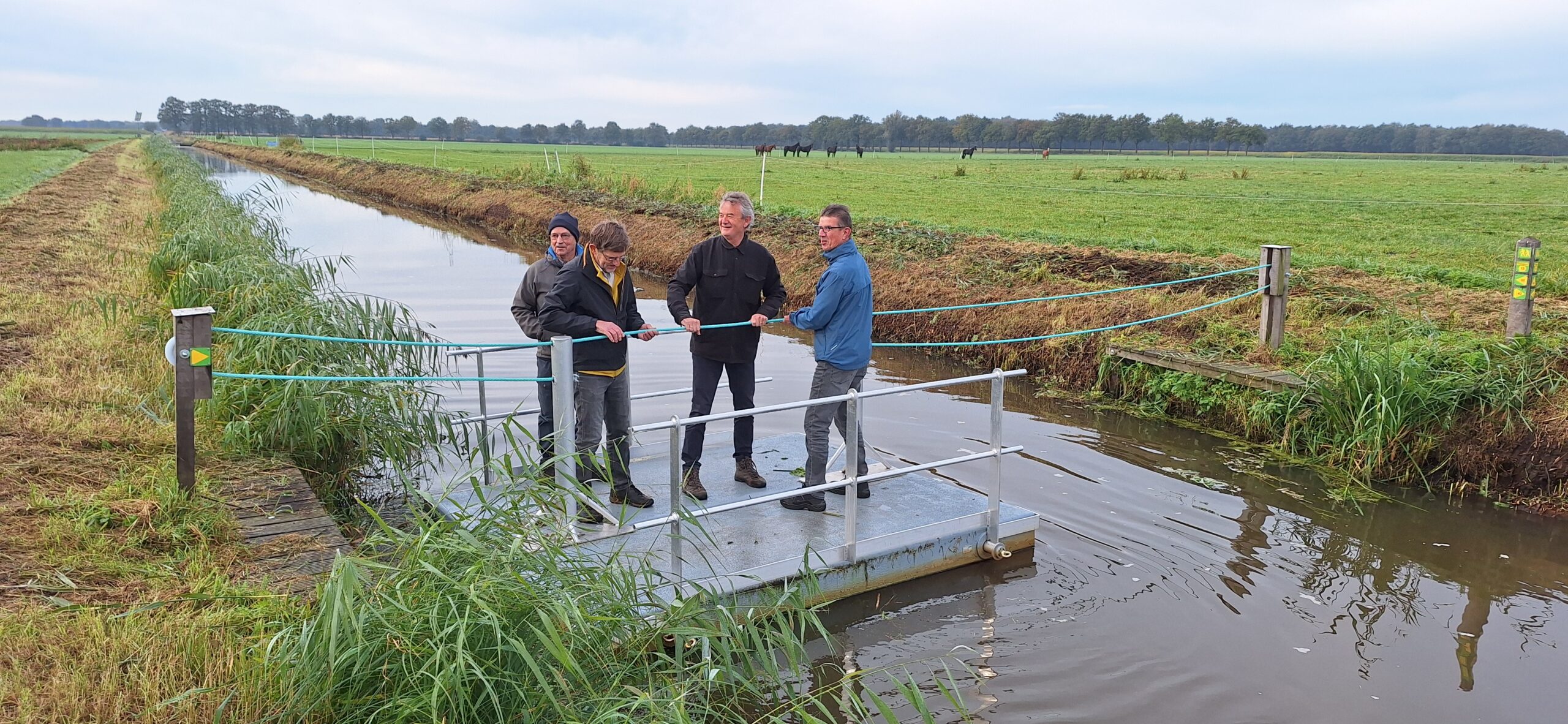 Vier mannen op een appelpontje over een brede sloot in een groen landschap.