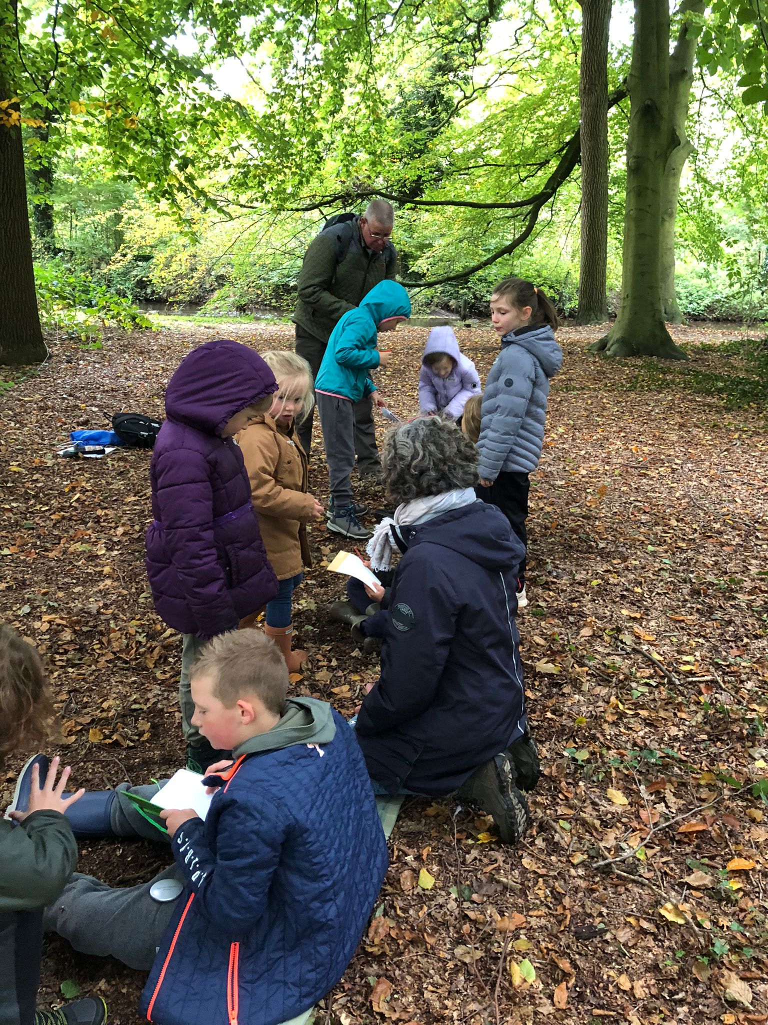 Kinderen en een volwassene doen buitenactiviteit in een bosrijke omgeving.