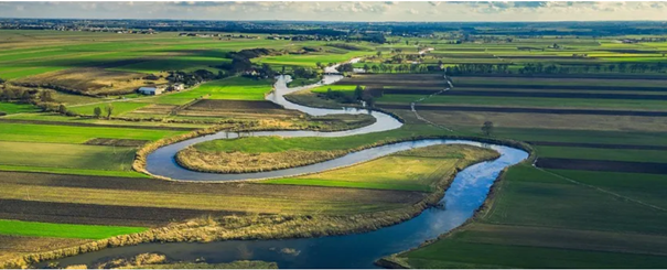 Kronkelende rivier door groene velden en akkers onder een bewolkte hemel.