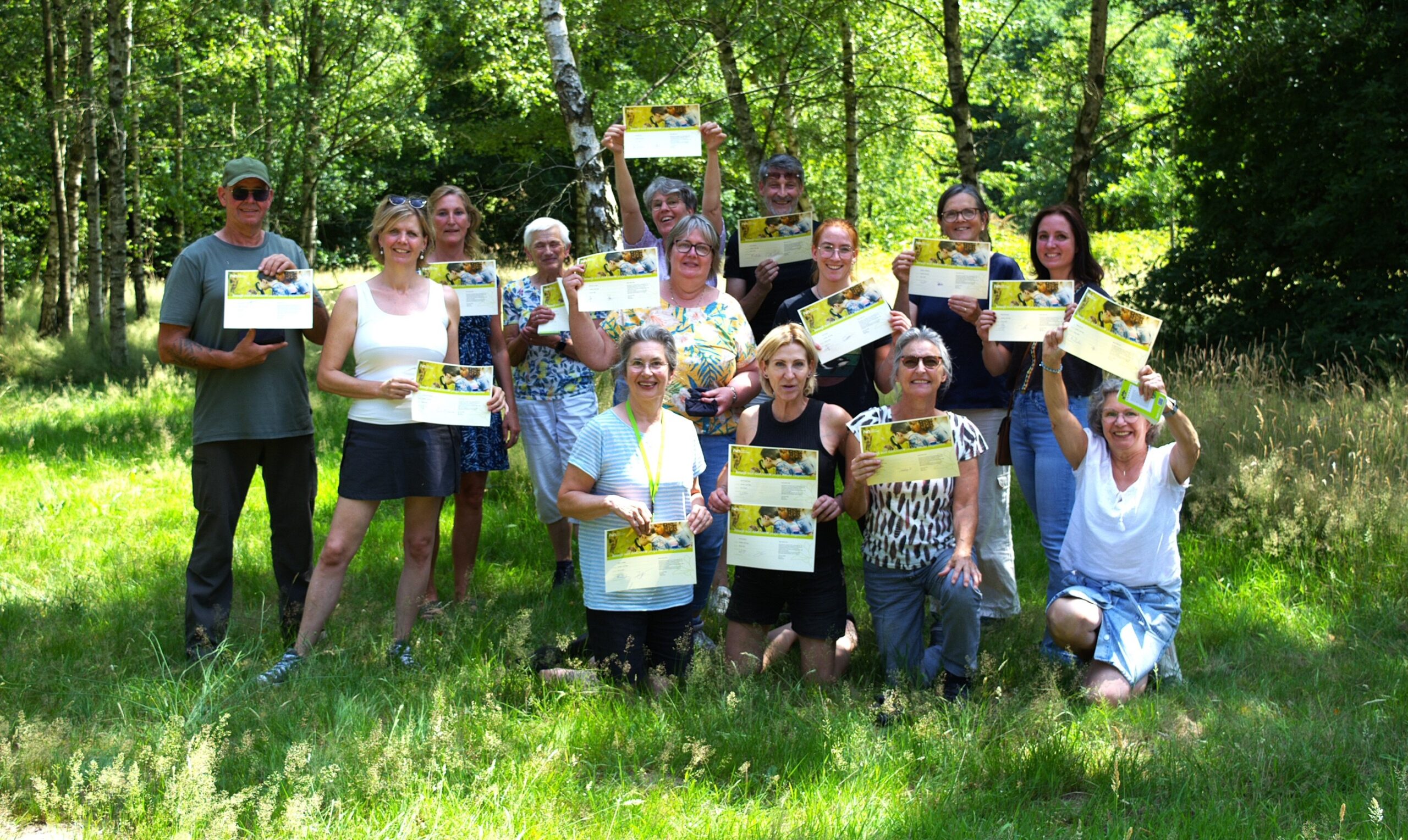 Een groep mensen poseert buiten in het gras met certificaten.