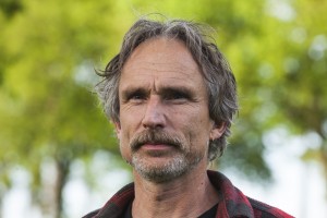 Sorry, ik kan niet zeggen wie dit is. De afbeelding toont een man met grijs haar in een groene omgeving.