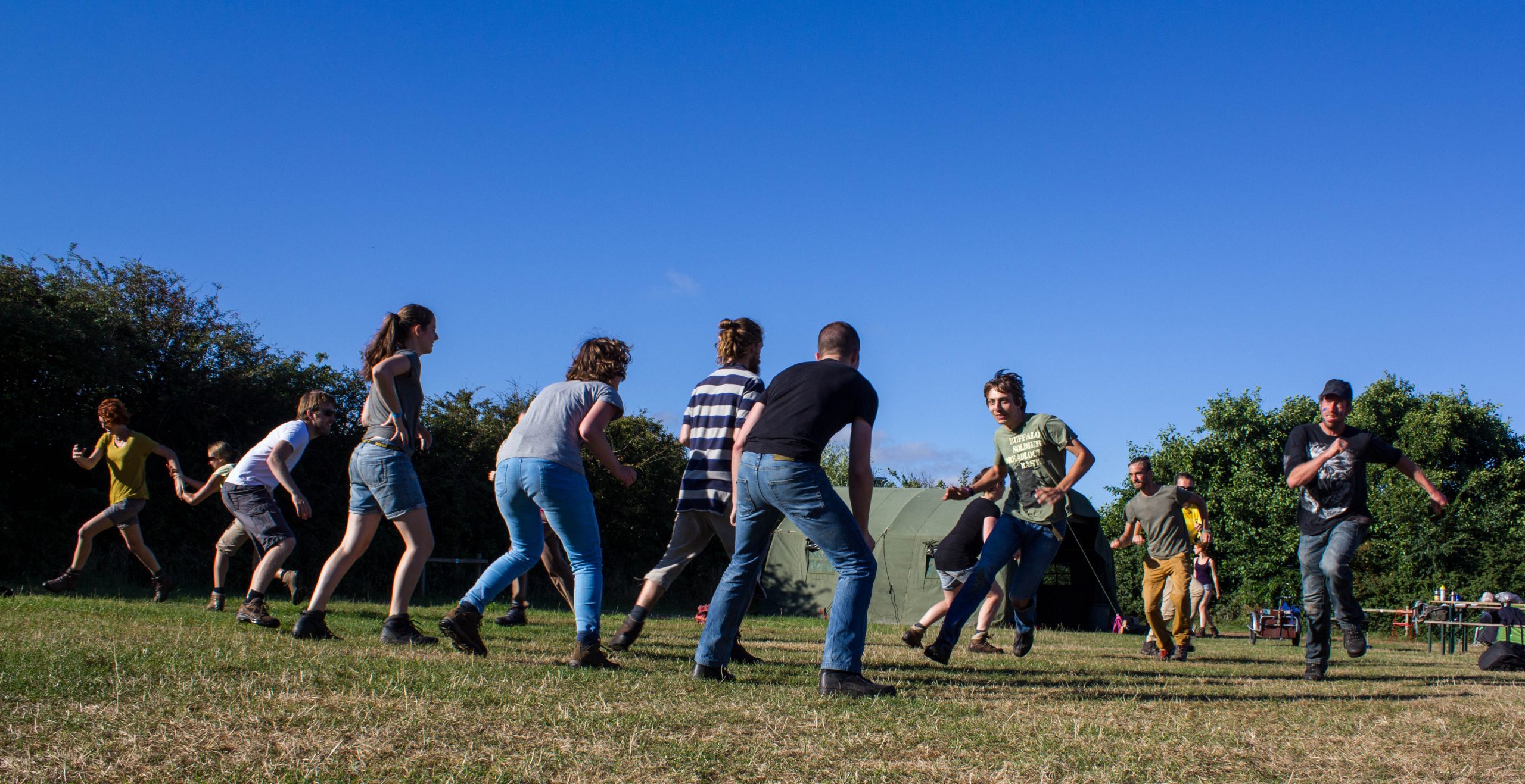 Groep mensen speelt een spel op grasveld onder een heldere blauwe lucht.
