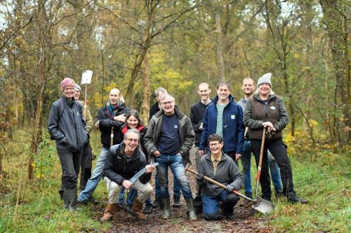 Groep mensen met schoppen in een bosrijke omgeving, mogelijk bezig met een natuurproject.