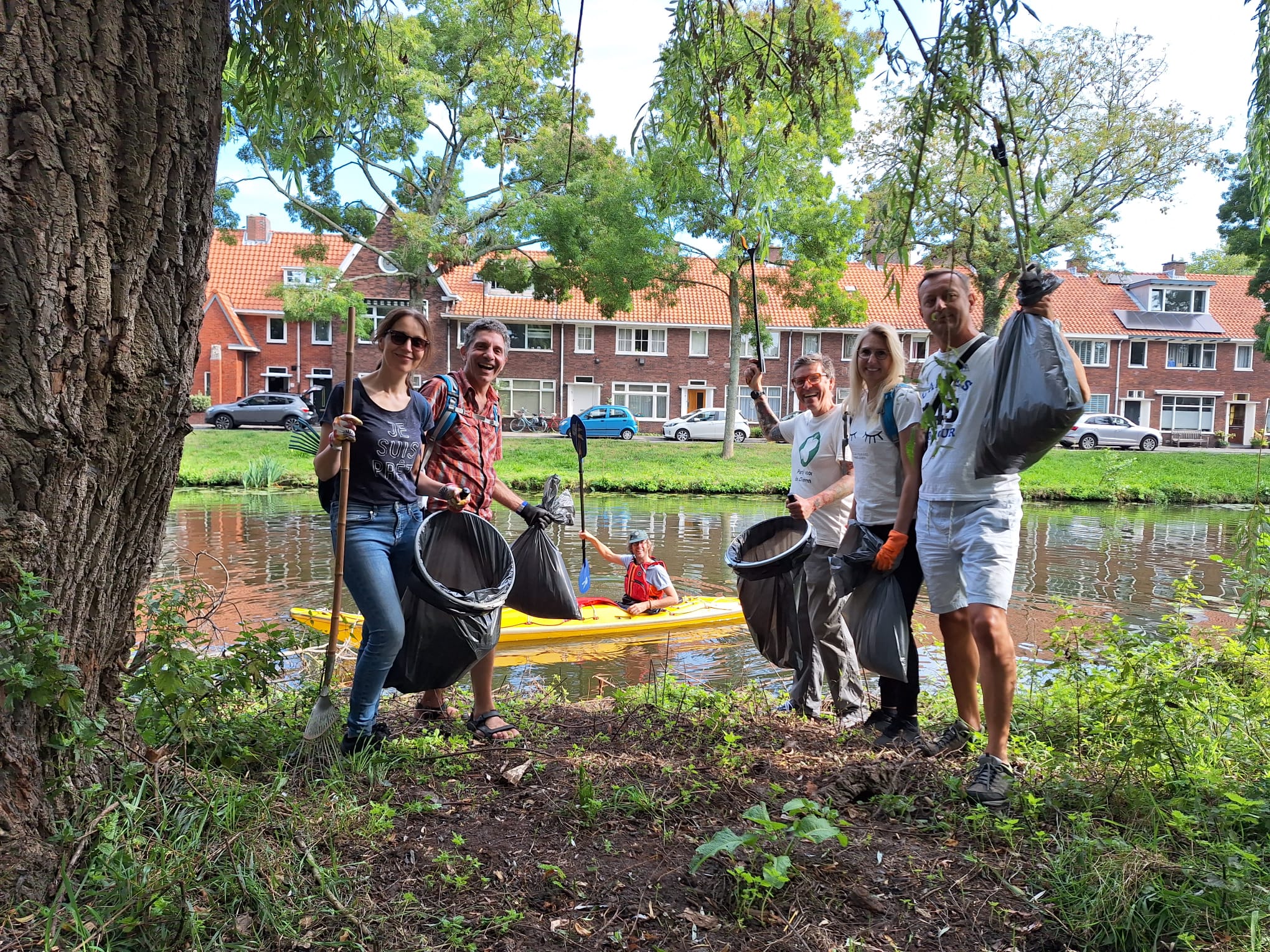 Foto van 7 mensen die afval opruimen: 6 op de waterkant met zakken troep en een man in de kano