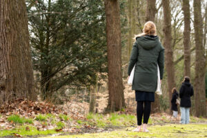 Vrouw loopt blootsvoets door een bos, met twee anderen verderop op het pad.