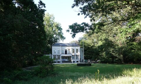 Wit herenhuis omringd door bomen met een groot gazon ervoor.