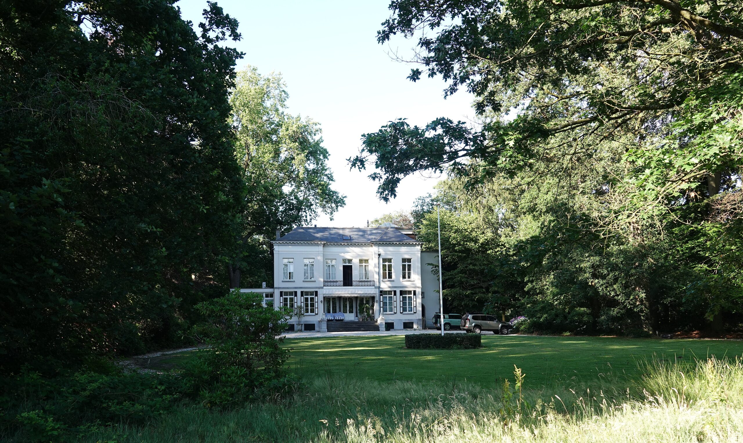 Wit herenhuis omringd door bomen met een groot gazon ervoor.