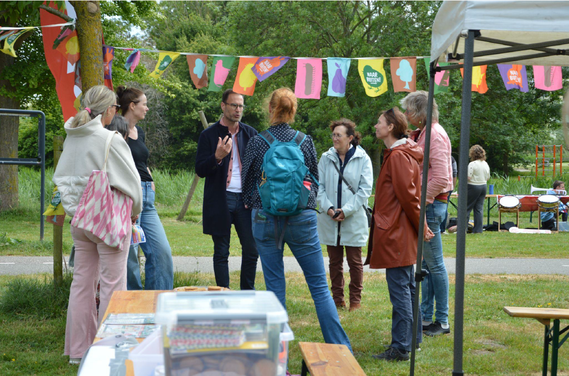Groep mensen in gesprek in een park, met kleurrijke vlaggetjes op de achtergrond.