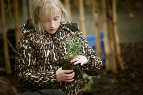 Kind in panterjas houdt een kleine plant vast, omringd door een natuurlijke, buitensetting.