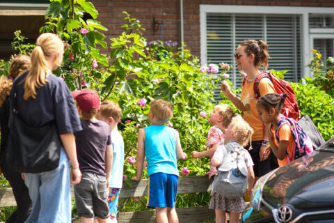 Kinderen en een volwassene bewonderen bloemen in een tuin op een zonnige dag.