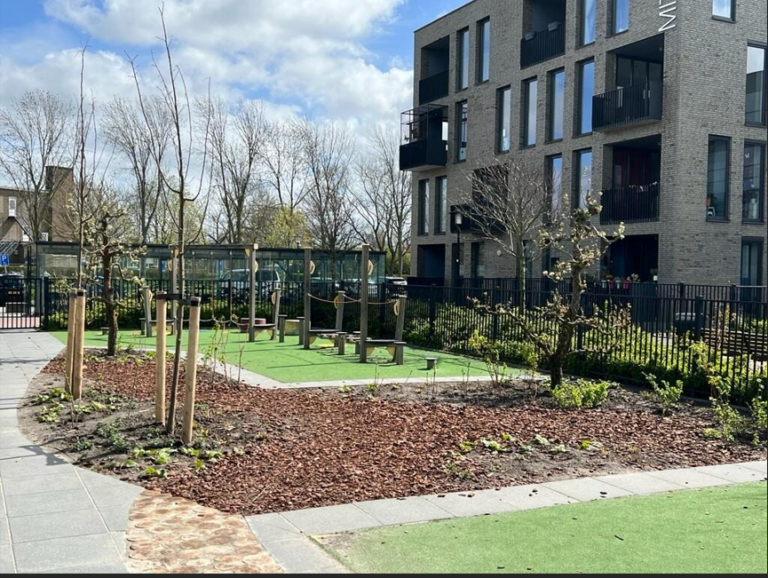 Moderne appartementen naast een kleine speeltuin met jonge boompjes en groenvoorzieningen.