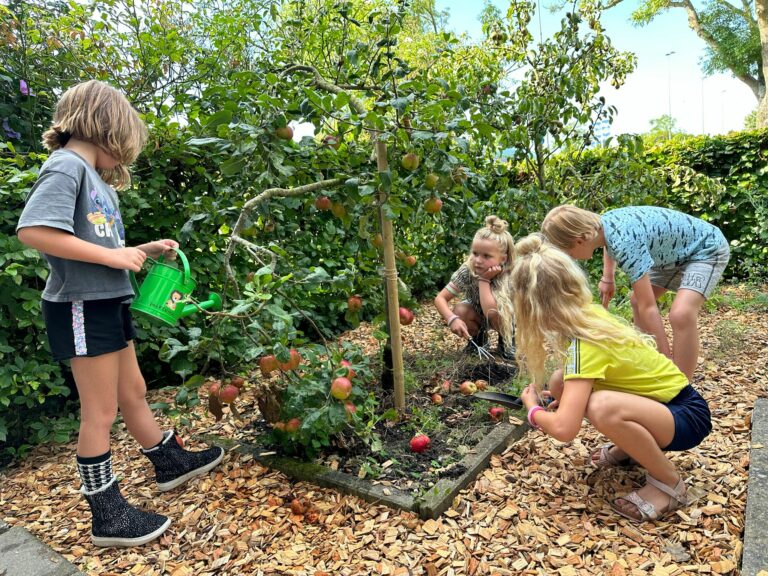 Kinderen verzorgen een kleine appelboom, met gieters en tuingereedschap in een groene tuin.