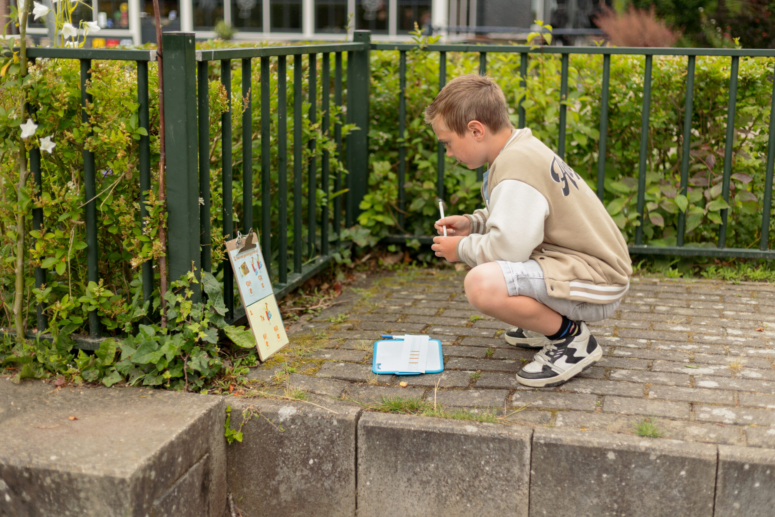 Kind squat naast een groen hek met een schrijfblok en notitieblok op de grond.