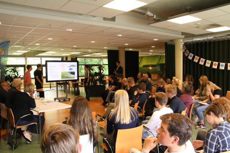 Een groep studenten houdt een presentatie voor een publiek in een klaslokaal.