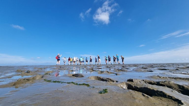 Groep mensen wandelt op een modderige vlakte onder een heldere blauwe lucht.
