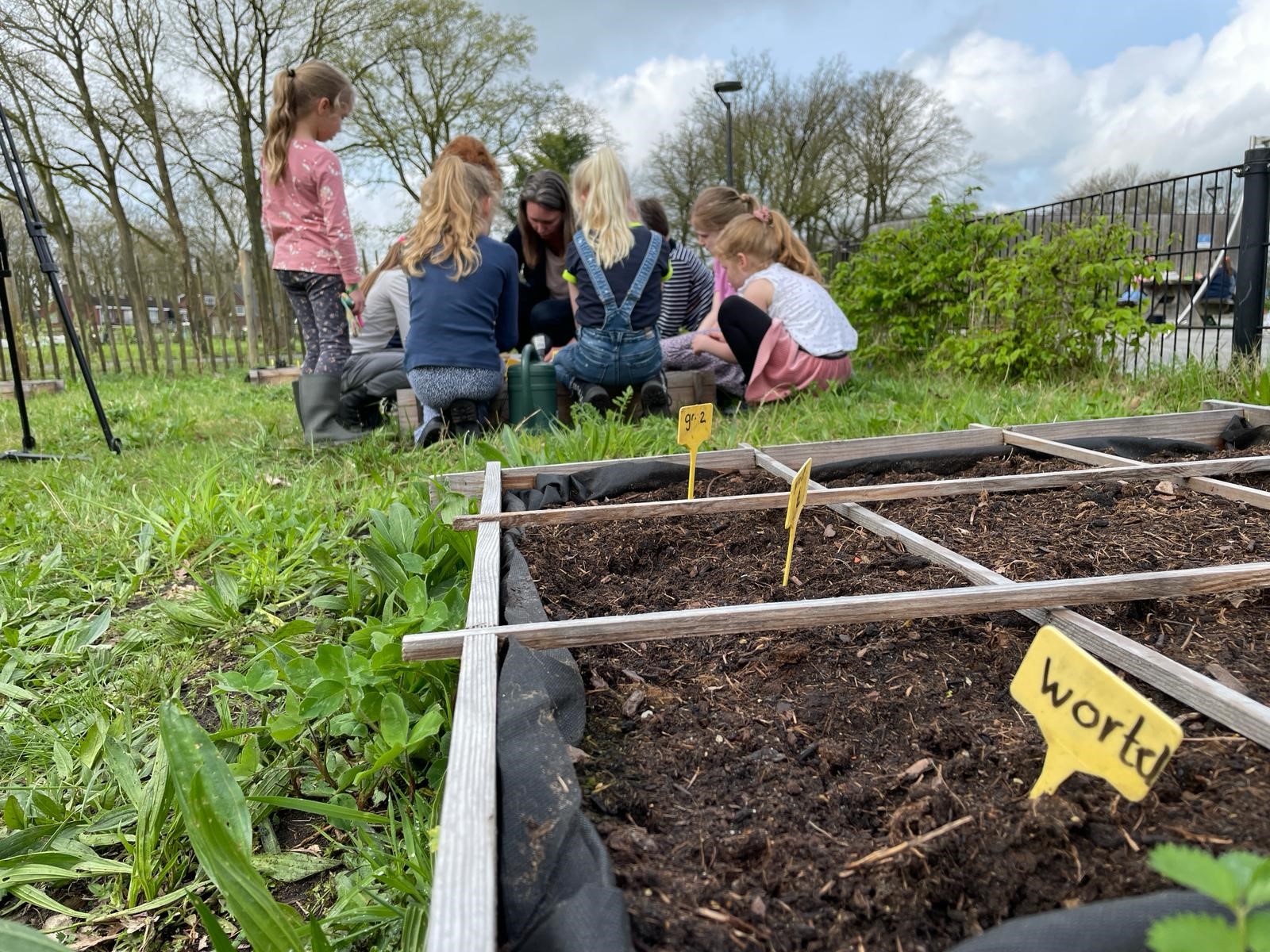 Kinderen werken samen in een moestuin, bij plantenbakken met zaaibordjes.