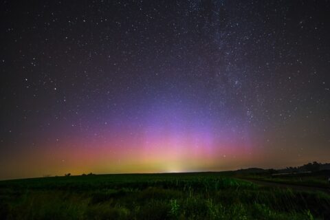 Sterrenhemel met kleurrijk poollicht boven een weelderig groen landschap.