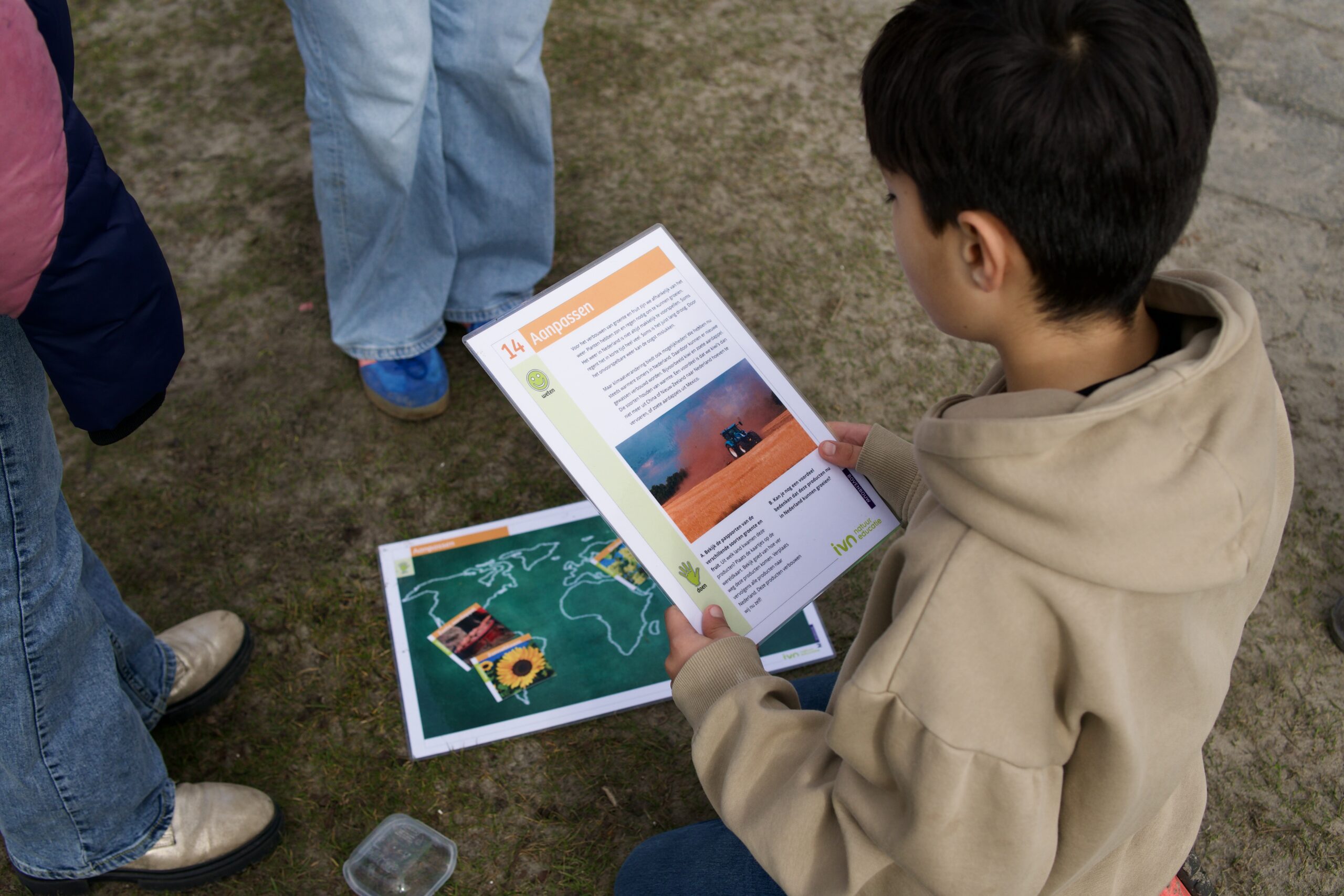 Een kind leest een informatiefolder met een foto over landbouw; andere folders op de grond.