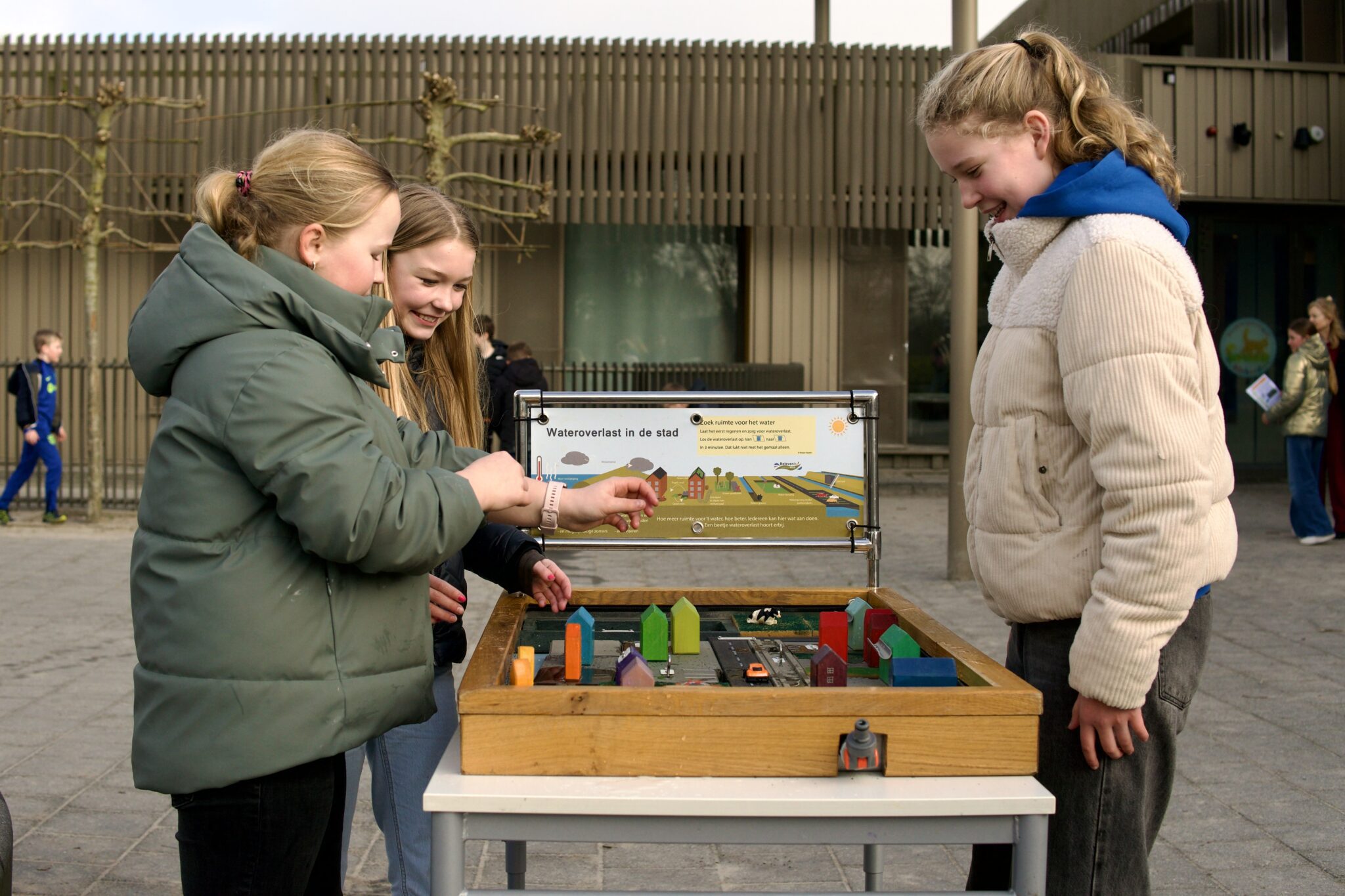 Drie kinderen onderzoeken een interactieve maquette over waterbeheer in een stedelijke omgeving.