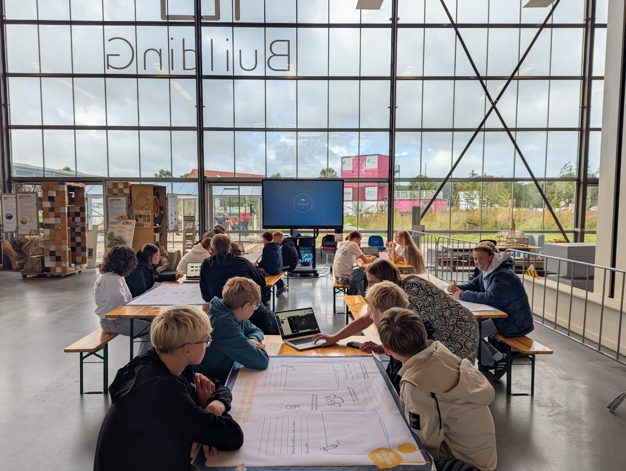 Een groep mensen werkt samen aan tafels in een ruim, licht gebouw met grote ramen.