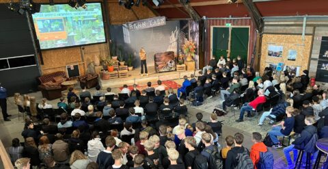 Een spreker presenteert in een volle zaal tijdens een 'Barn Talk'.