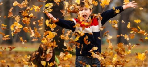Twee kinderen spelen enthousiast met vallende herfstbladeren in een park.