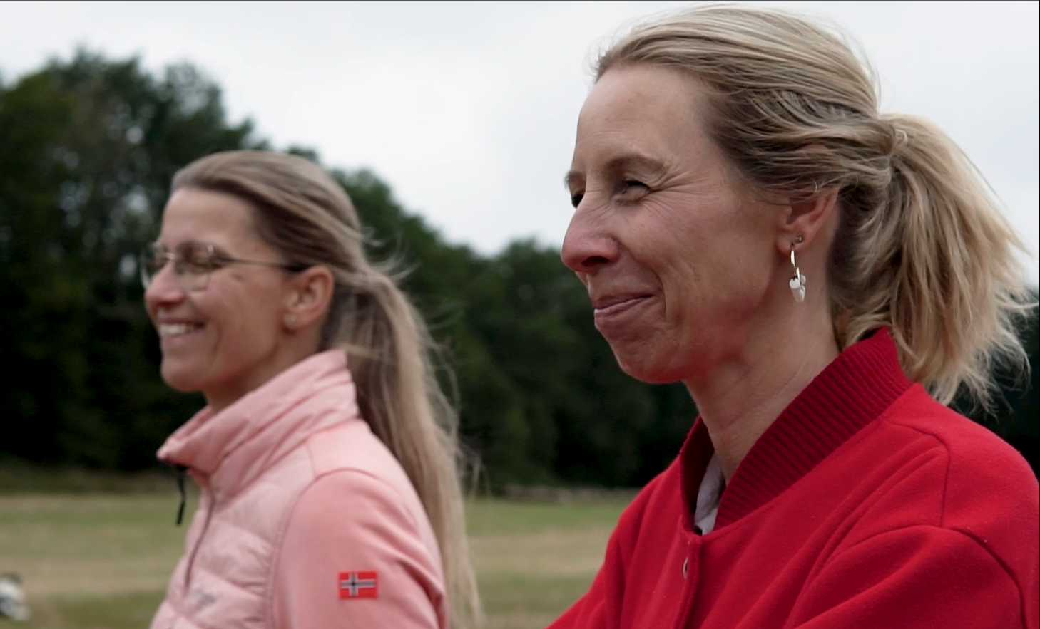 Twee lachende vrouwen in sportkleding buiten, met een bos op de achtergrond.