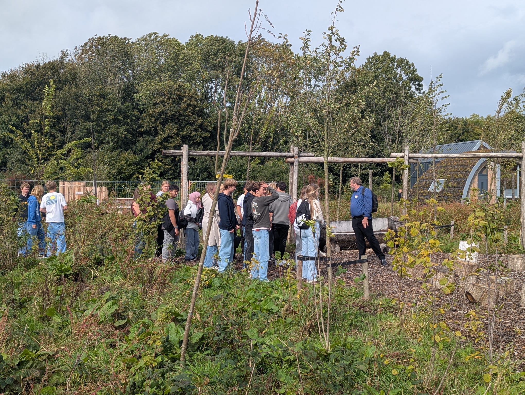 Groep mensen in een groene, open tuin met houten constructie en bomen.